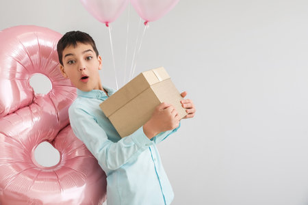 Surprised little boy with gift box and balloons on light background. International Women's Day