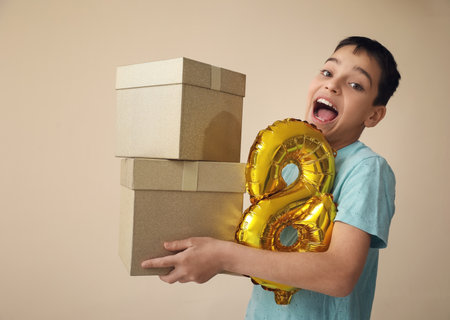 Little boy with balloon in shape of figure 8 and gift boxes on beige background. International...