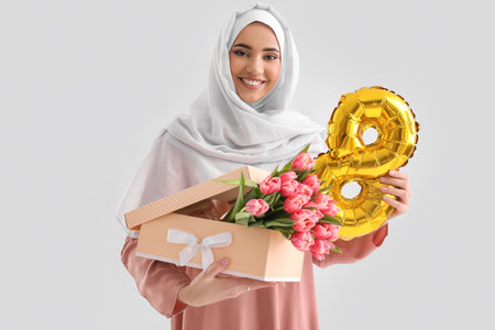 Muslim woman with gift box, tulips and balloon on light background. International Women's Day