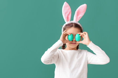 Funny little girl with bunny ears and Easter eggs on green background