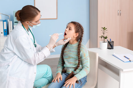 Doctor examining little girl with sore throat in clinicの写真素材