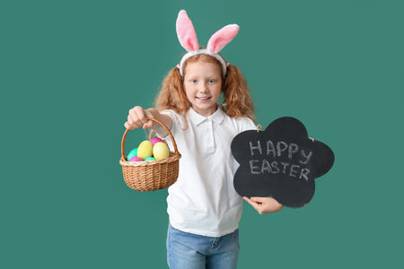 Funny little girl with bunny ears, board and Easter basket on green background