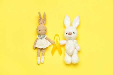 Toy rabbits with golden awareness ribbon on yellow background. International Childhood Cancer Dayの写真素材