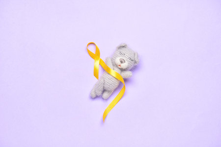 Golden awareness ribbon and toy bear on violet background. International Childhood Cancer Dayの写真素材