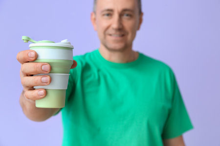 Mature man in green t-shirt with cup of coffee on lilac background, closeupの写真素材