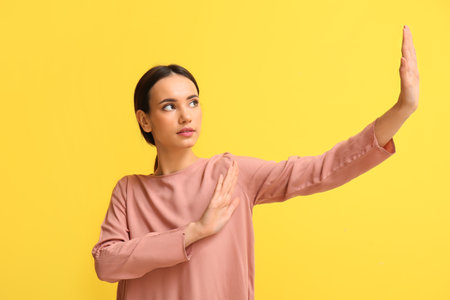 Young woman showing stop gesture on yellow background. immunity conceptの写真素材