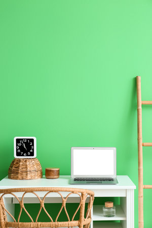 Modern workplace with laptop and clock near green wallの写真素材