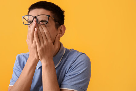 Young Asian man worrying on yellow background