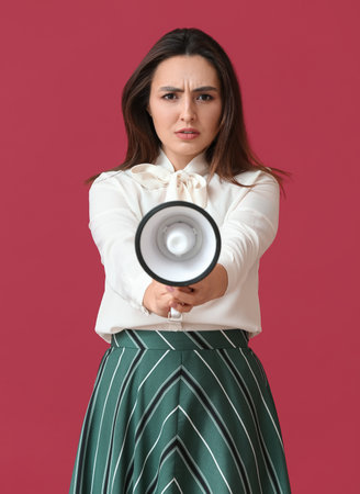 Angry young woman with megaphone on color backgroundの写真素材