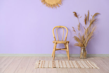 Wicker chair and vase with reed flowers near violet wall in room interiorの写真素材
