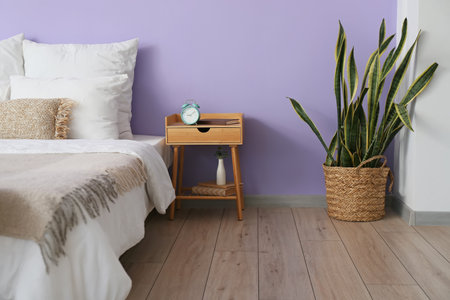 Bed and bedside table near violet wall in stylish roomの写真素材