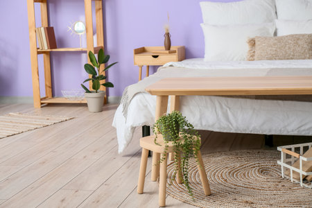 Houseplant on wooden stool near bed in stylish bedroom interior