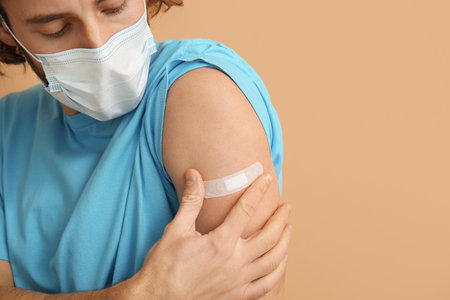 Young man in medical mask after vaccination on color background