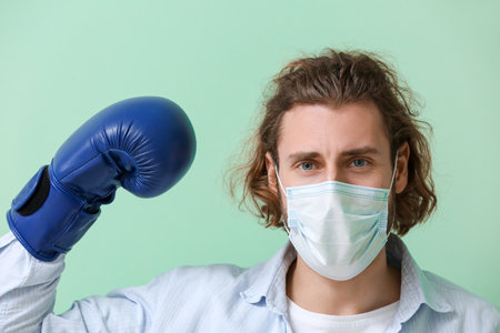 Young man wearing medical mask and boxing gloves on color background. concept of strong immunityの写真素材
