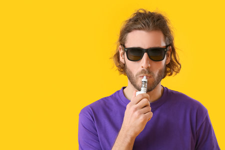 Vaping young man on yellow backgroundの写真素材