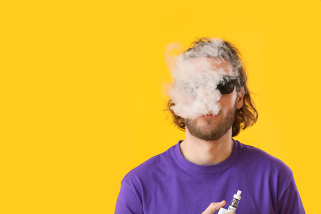 Vaping young man on yellow backgroundの写真素材