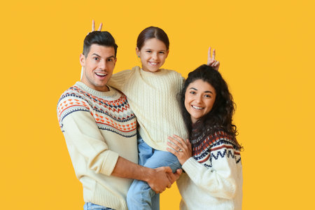 Happy parents with little daughter in warm sweaters on yellow backgroundの写真素材