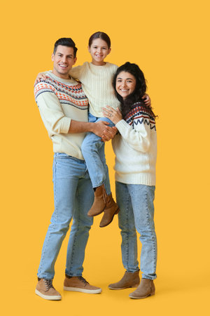 Happy parents with little daughter in warm sweaters on yellow backgroundの写真素材