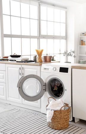 Modern washing machine and laundry basket in light kitchenの写真素材