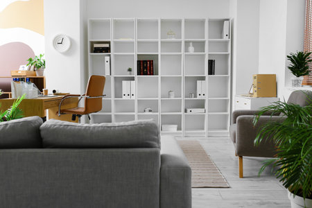 Interior of office with shelving unit, workplace and stylish clock on light wall