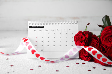 Calendar with roses, ribbon and hearts on table against white wooden background. Valentine's Day celebrationの写真素材