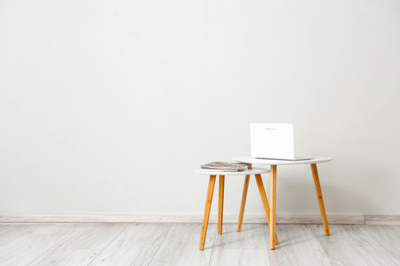 Small tables with laptop and magazines near light wallの写真素材