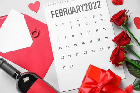 Calendar with bottle of wine, envelope, rings, gift and roses on light background. Valentine's Day celebrationの写真素材