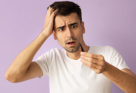 Worried young man with fallen down hair on lilac background
