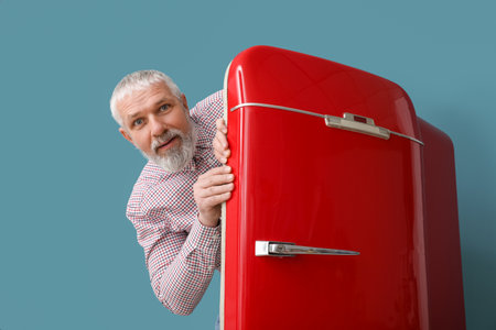 Mature man and red fridge on blue backgroundの写真素材