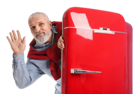 Mature man with red fridge waving hand on white backgroundの写真素材