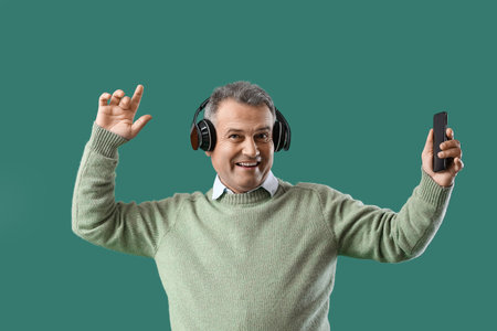 Senior man in headphones with mobile phone dancing on green backgroundの写真素材
