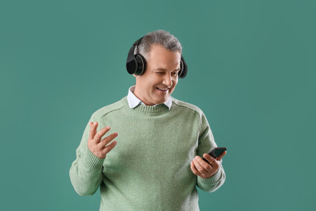 Senior man in headphones using mobile phone on green background