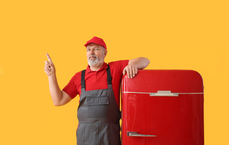 Mature worker with retro fridge pointing at something on yellow backgroundの写真素材