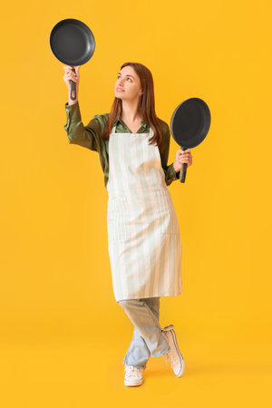 Pretty young woman with frying pans on yellow backgroundの写真素材