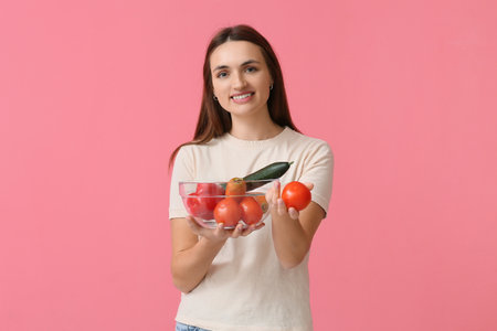 Pretty young woman holding bowl with fresh vegetables on pink backgroundの写真素材