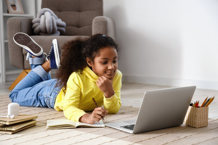 Little African-American girl studying with online tutor on floor at home