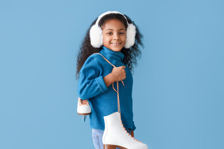 Little African-American girl in earmuffs with ice skates on blue backgroundの写真素材