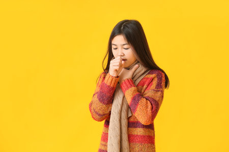 Ill Asian girl with sore throat on color backgroundの写真素材