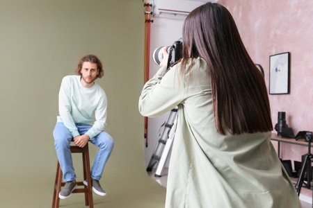 Female photographer taking picture of young man in studio