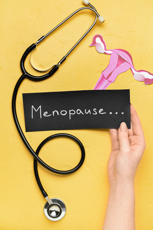 Woman holding paper with word MENOPAUSE, stethoscope and uterus on yellow backgroundの写真素材