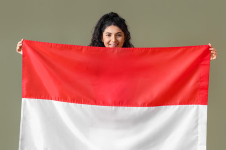 Beautiful smiling Asian woman with big flag of Indonesia on color backgroundの写真素材