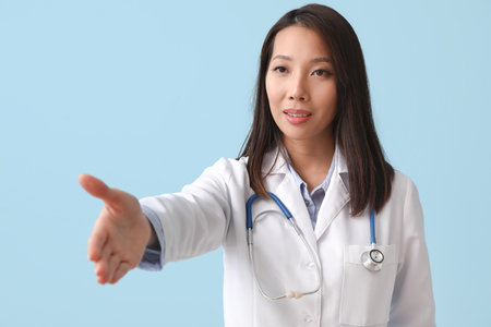 Female Asian doctor giving hand for shake on blue backgroundの写真素材