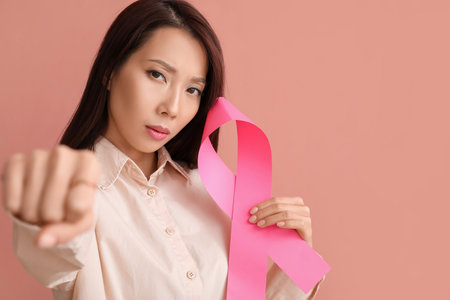 Young Asian woman with pink ribbon on color background. breast cancer awareness conceptの写真素材