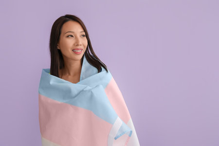 Young Asian woman with transgender flag on lilac backgroundの写真素材