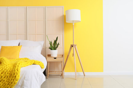 Comfortable bed, folding screen, lamp and houseplant on nightstand near color wallの写真素材