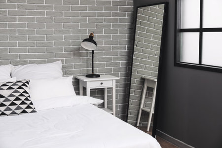 Comfortable bed, mirror and modern lamp on nightstand in room
