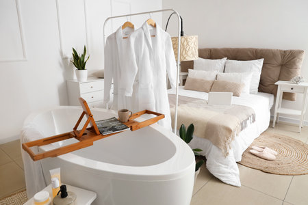 Interior of light bedroom with bathtub, rack and bathrobesの写真素材