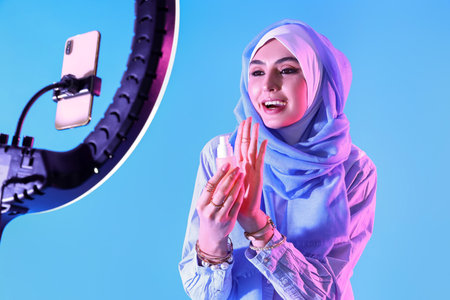 Muslim beauty blogger with makeup foundation recording video on blue backgroundの写真素材