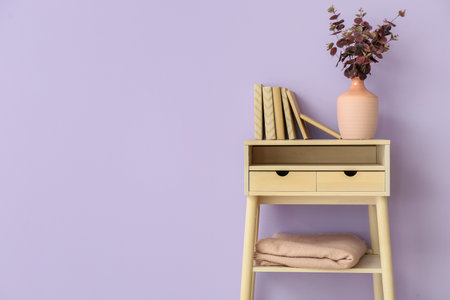Vase with eucalyptus branches and books on table near violet wallの写真素材