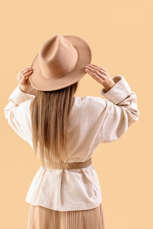 Beautiful fashionable young woman in hat and knitted sweater on beige background, back viewの写真素材